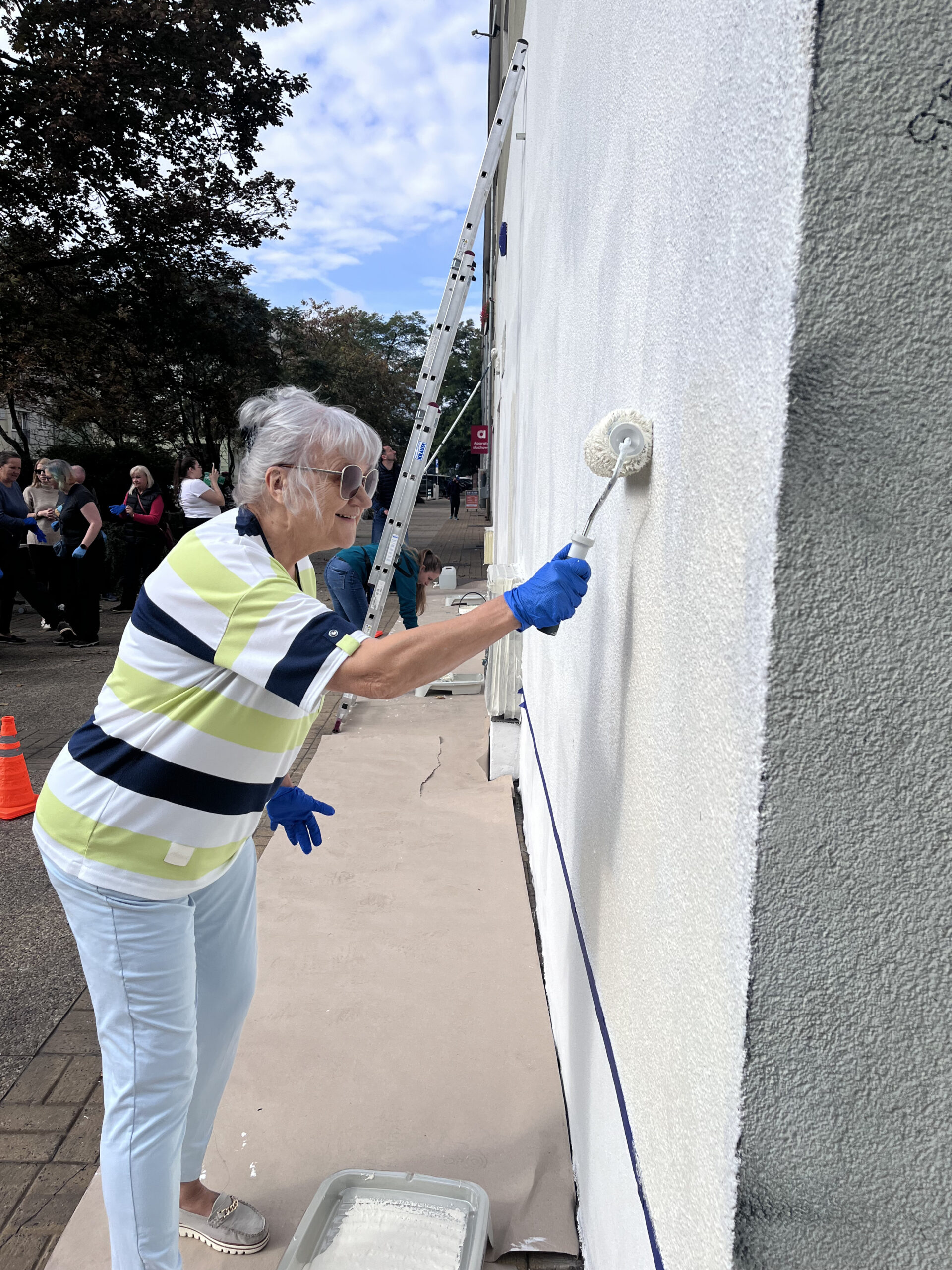 Zdjęcie przedstawia kobietę malującą ścianę Centrum Aktywności i Wolontariatu Seniorów