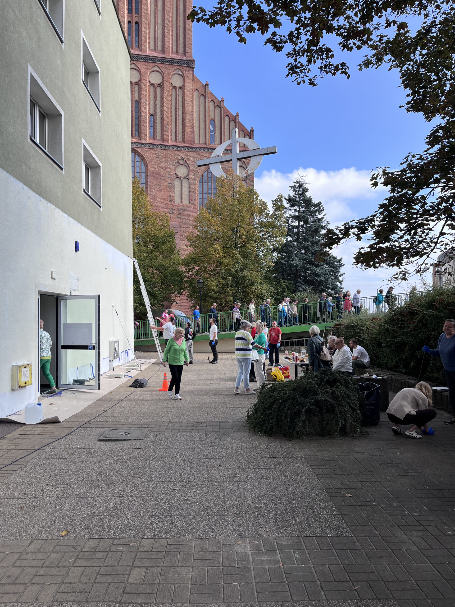 Zdjęcie przedstawia ludzi podczas akcji społecznej pod Centrum Aktywności i Wolontariatu Seniorów